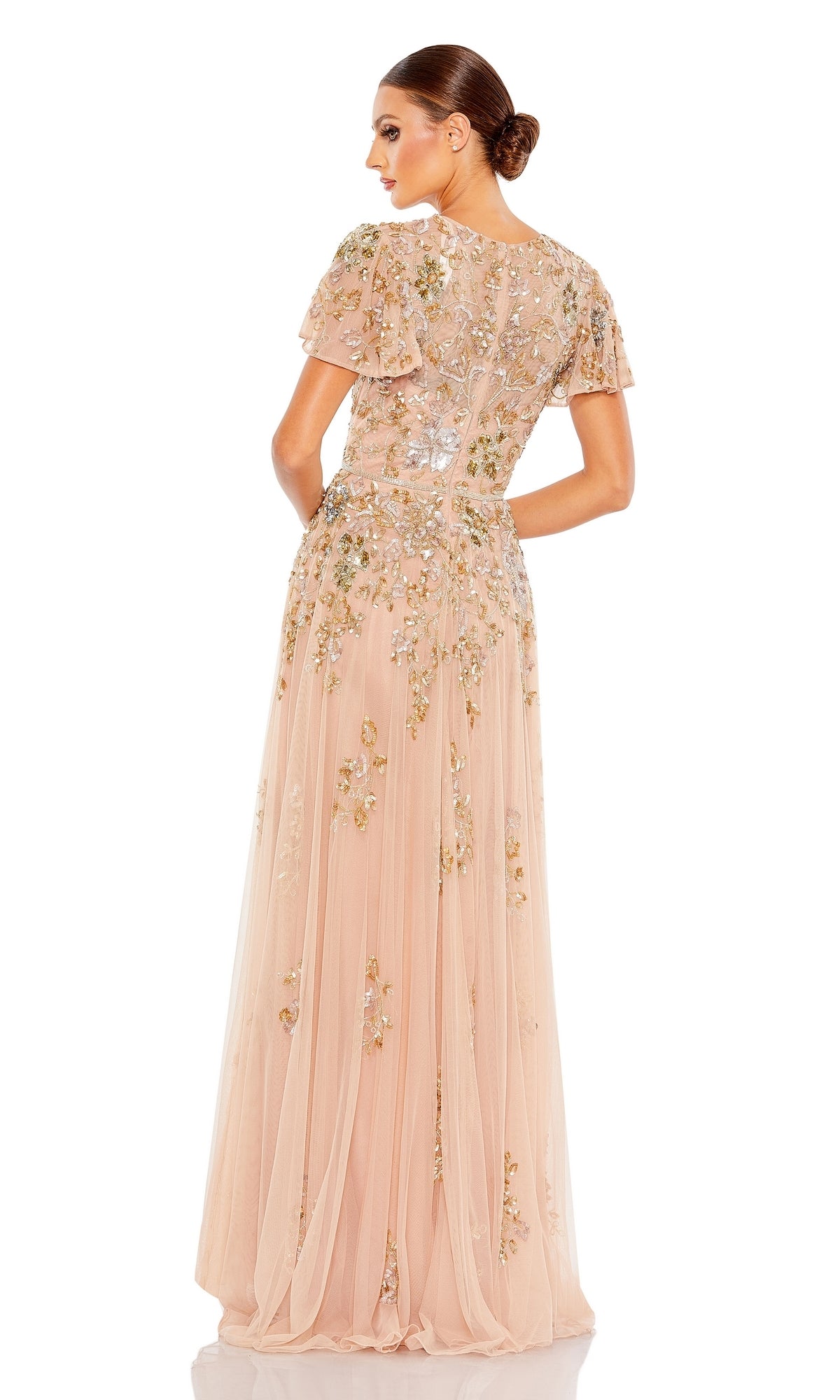 Woman wearing the Mac Duggal 5717 Short Sleeve Beaded Formal Dress, a light pink, floor-length gown with floral sequin embellishments, stands with her back to the camera.